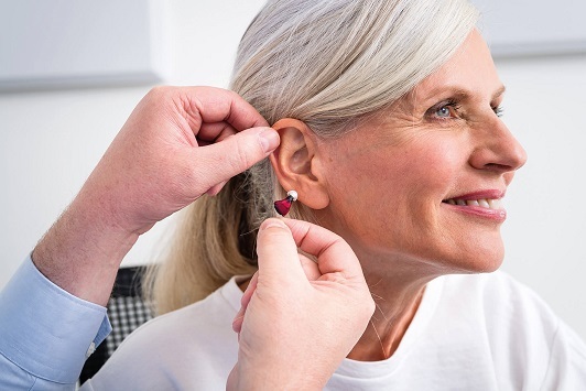 Ältere Frau bekommt ein modernes Hörgerät eingesetzt und lächelt zufrieden beim Hörtest.